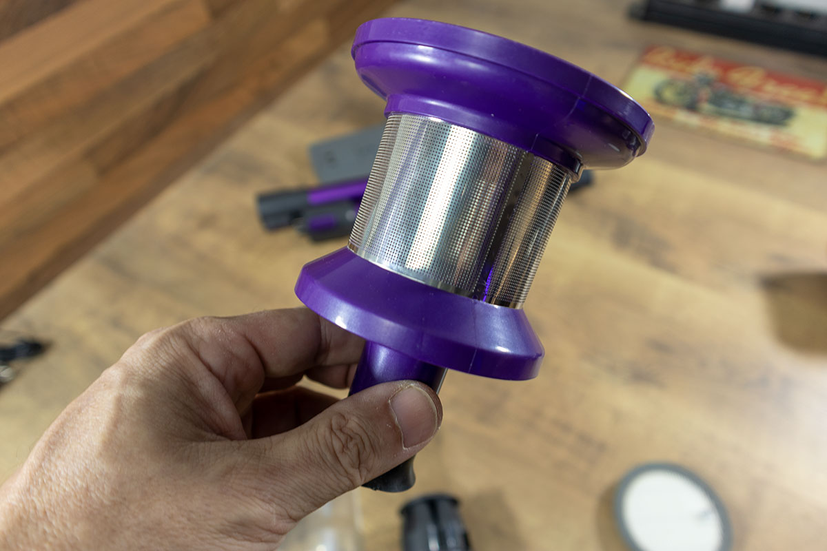 a hand holding a purple and silver vacuum cleaner filter